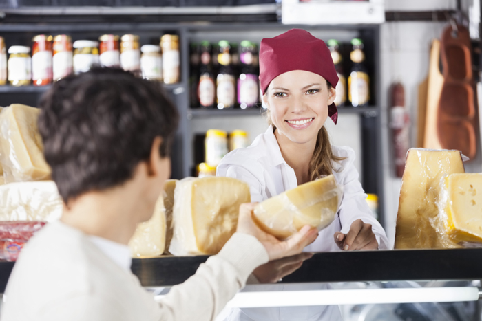 Smiling young saleswoman selling cheese to man in grocery store